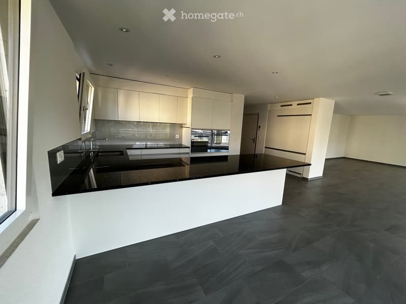 Modern kitchen with white cabinets, black countertops, and a central island. Features a sink with a faucet and a dark tiled floor.