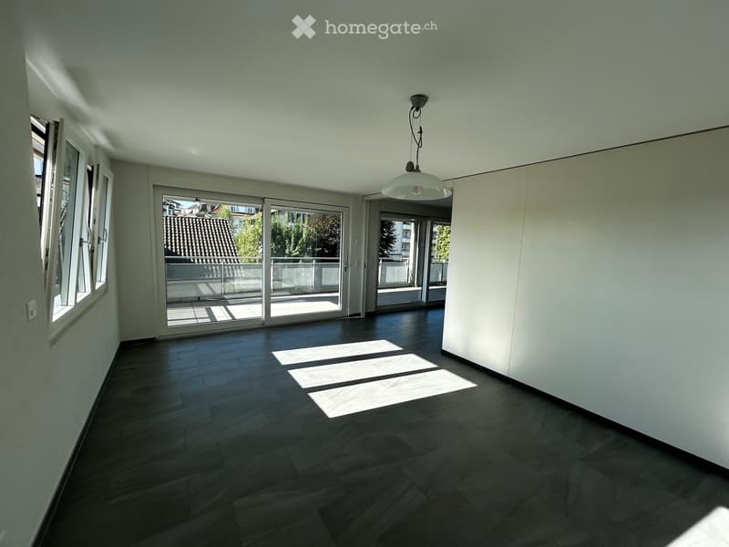 Empty room with dark wooden flooring, white walls, large windows, and sliding glass doors leading to a balcony.