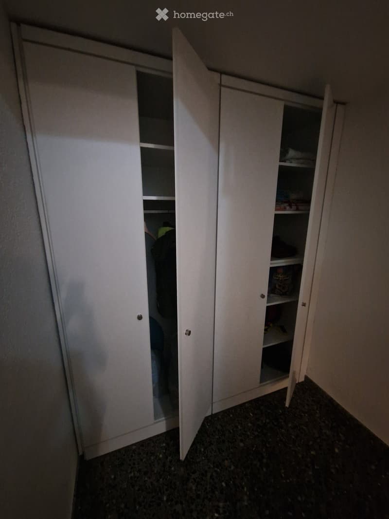 Empty room with white built-in wardrobes, dark tiled floor, and exposed beams on the ceiling.