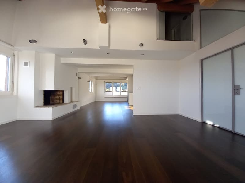 Empty room with dark hardwood flooring, white walls, and a built-in fireplace. The space features recessed lighting and large windows allowing natural light to enter.