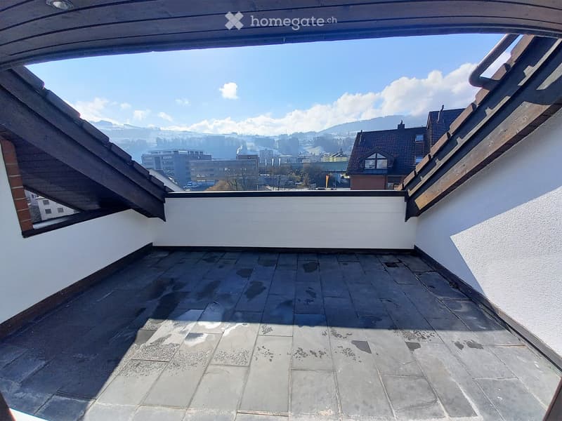Roof terrace with tiled flooring, white walls, and a panoramic view of a town and mountains under a clear blue sky.