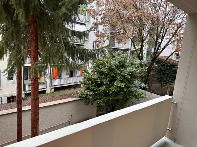Balcony overlooking a residential area with trees and neighboring buildings. The balcony has a wooden deck and white railings.