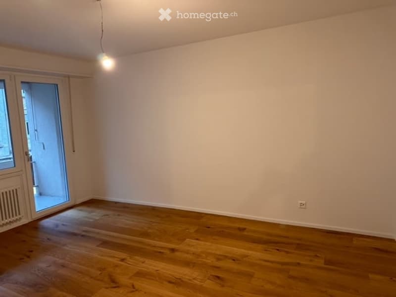 Empty room with wooden flooring, white walls, and a large sliding glass door leading to a balcony.