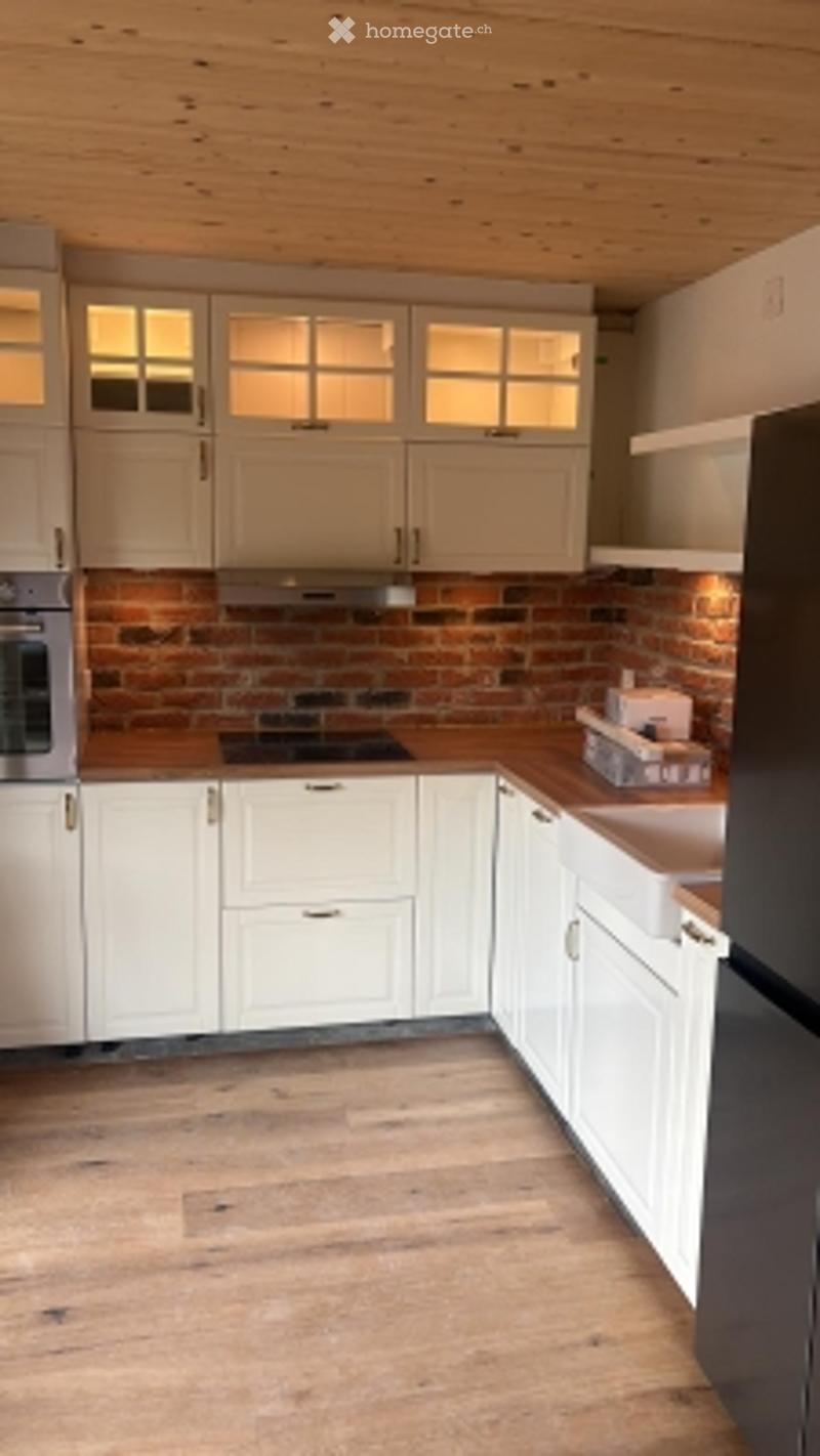 Modern kitchen with white cabinets, a brick backsplash, and wooden flooring. Features an oven, stove, refrigerator, and sink.