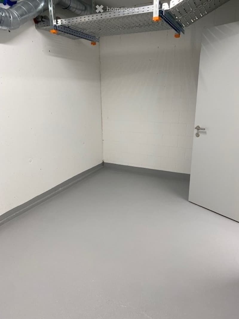 Empty room with white walls, grey floor, and a white door. No furniture or equipment present.