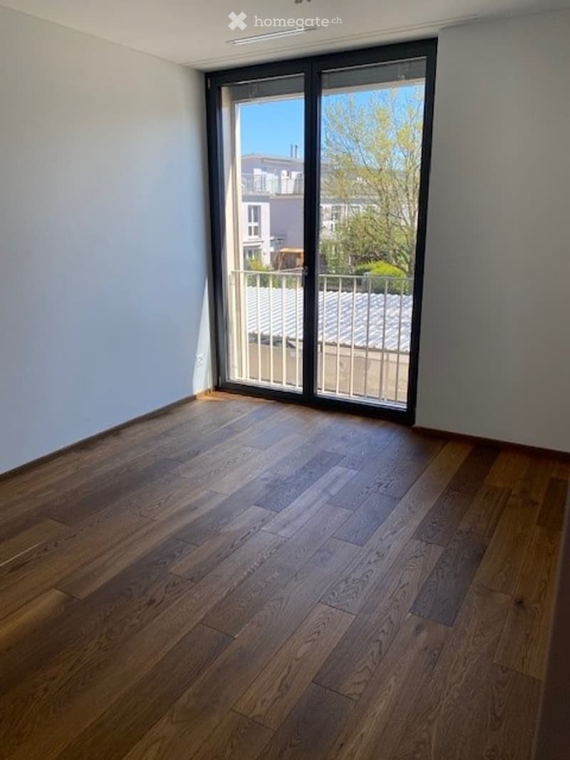 Empty room with wooden flooring and large sliding glass door leading to a balcony.