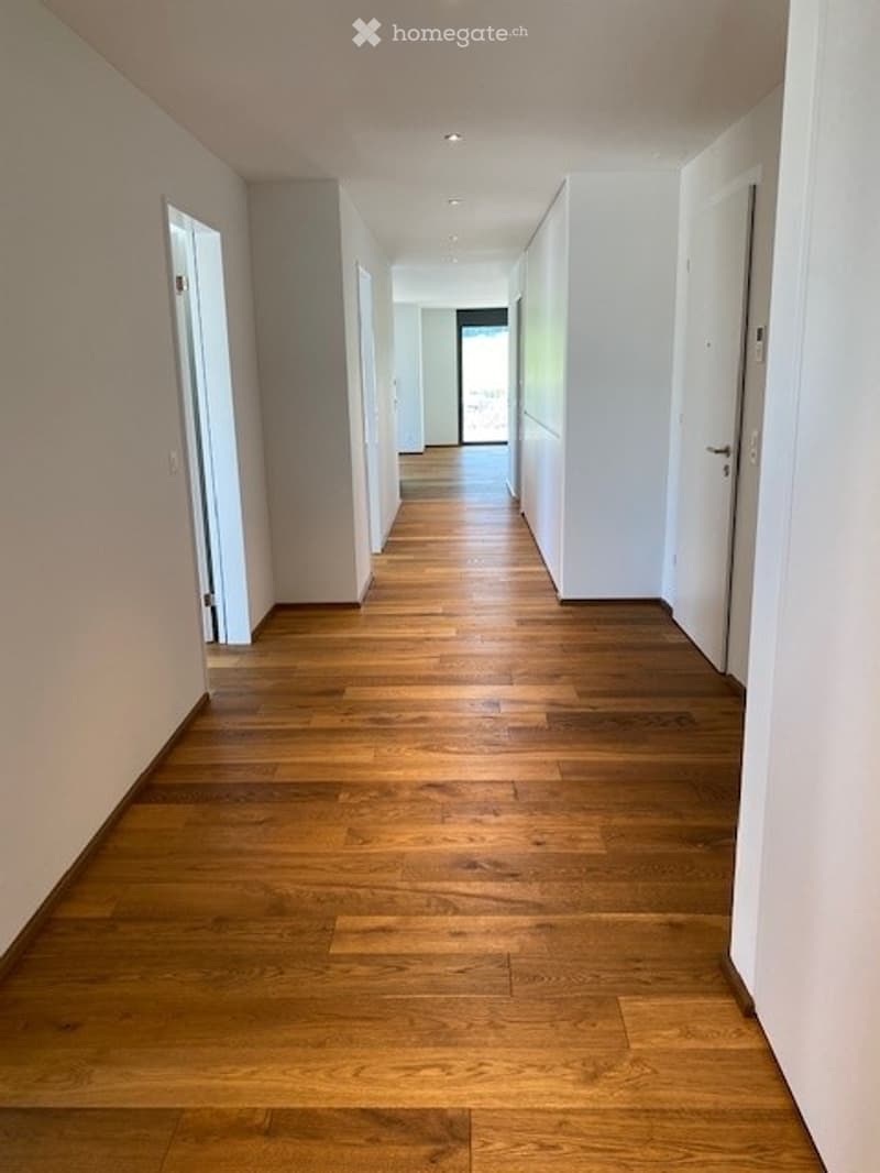 Empty hallway with wooden flooring and white walls, leading to an open doorway at the end.