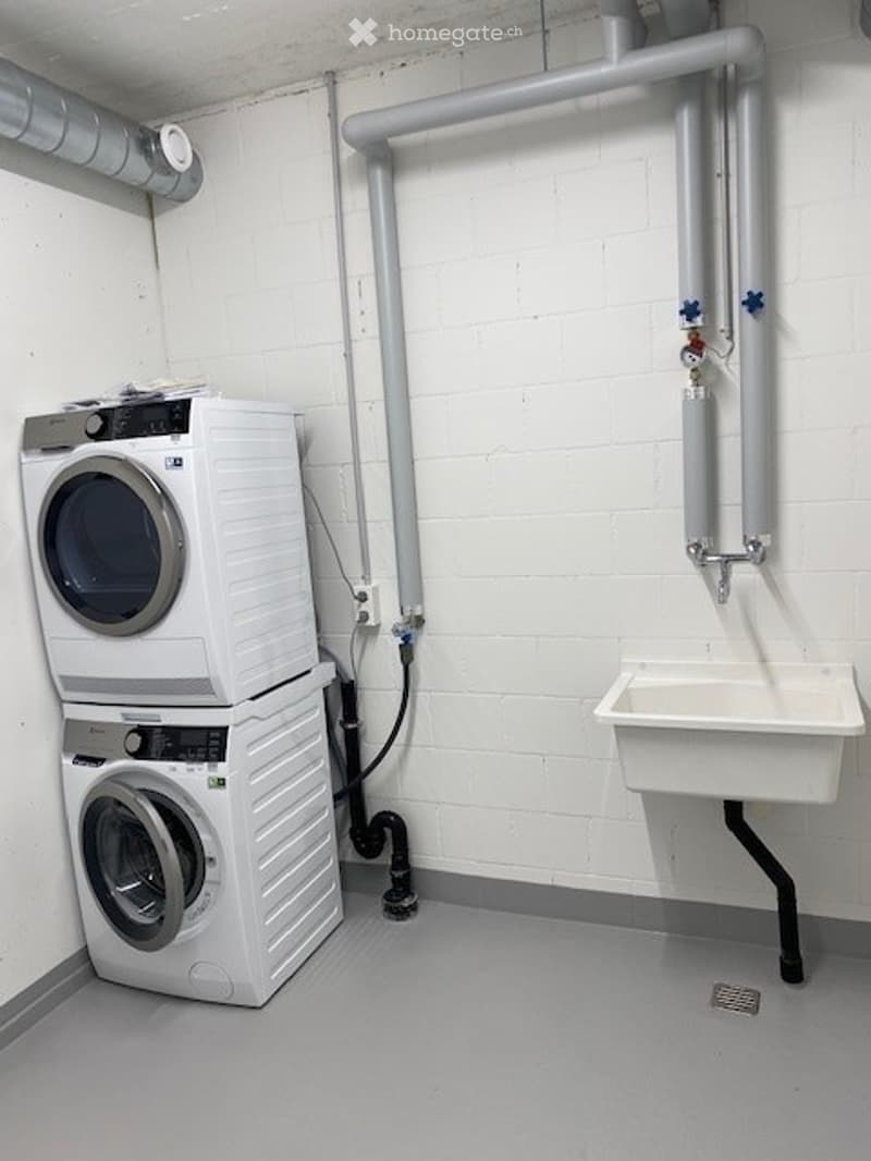 Laundry room with stacked washer and dryer, white brick walls, and a small sink.