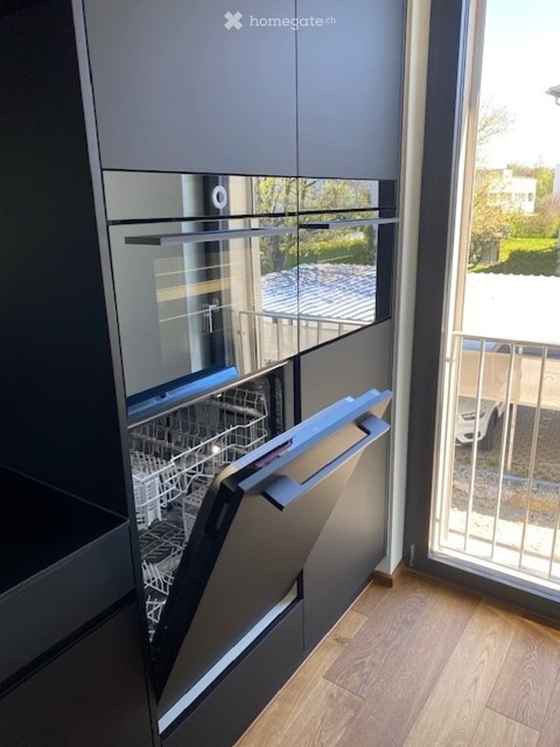 Modern kitchen with dark grey cabinets, a built-in dishwasher, and a large window overlooking a balcony area.