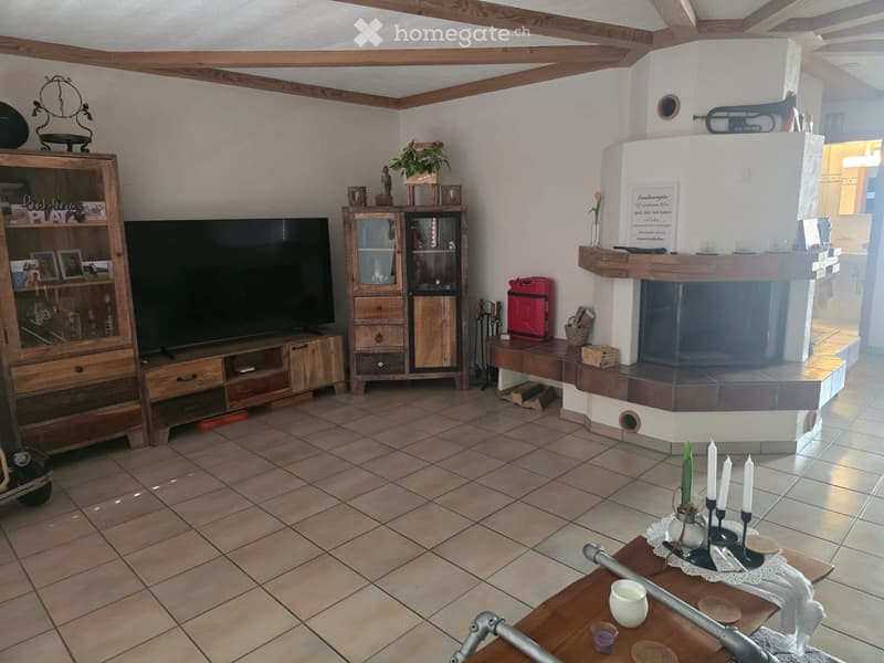 Living room with exposed wooden beams, tiled floor, fireplace, television, wooden cabinet, coffee table, and decorative items.