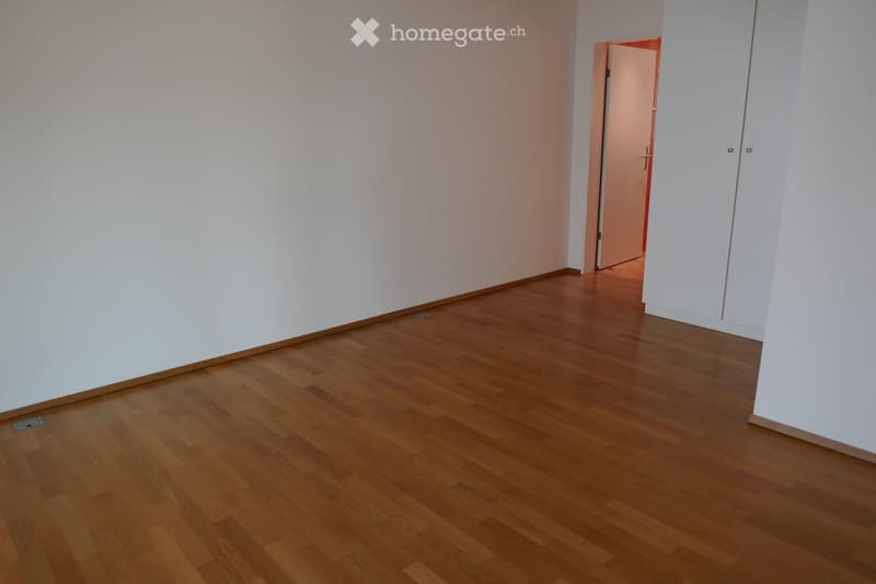 Empty room with light-colored walls and wooden flooring, featuring a partially open door leading to another space.