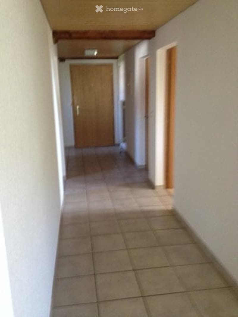 Empty hallway with tiled floor, white walls, wooden ceiling, and two doors.
