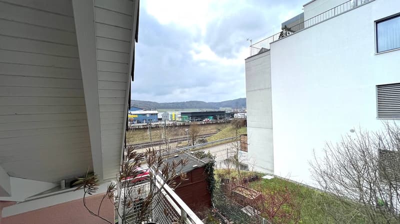 Balcony with railings, view of a road, a red car, a building, and a mountain range