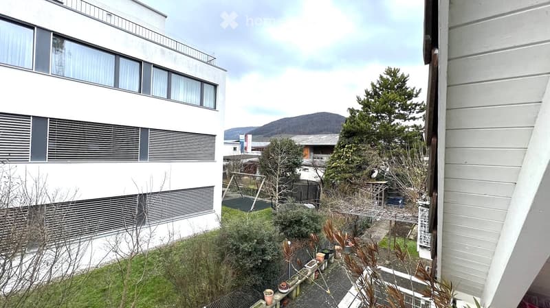 Exterior view, modern building, fenced yard, grass lawn, trees, mountains in the background