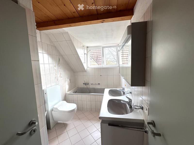 Bathroom with bathtub, double sink, toilet, white tiles, wooden ceiling, window
