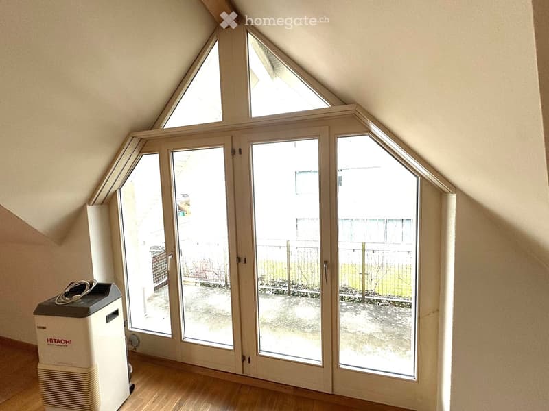 A room with wooden floor, white walls, large glass doors, and a view of the outside