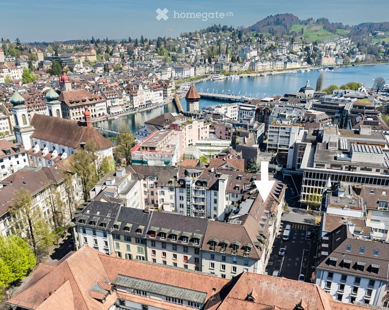 Aerial view of a cityscape with numerous buildings, red-tiled roofs, and a waterfront with boats and a bridge.