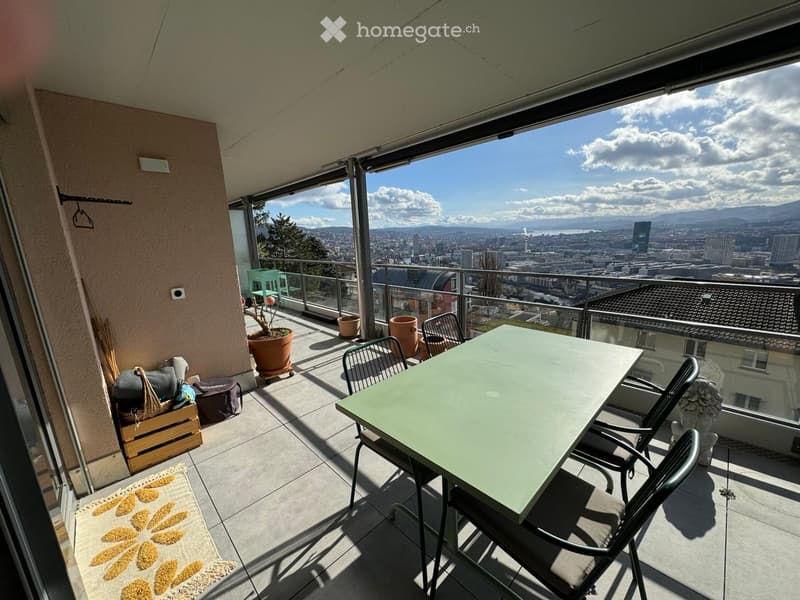 Balcony with a cityscape view, featuring a table, chairs, potted plants, and a rug.