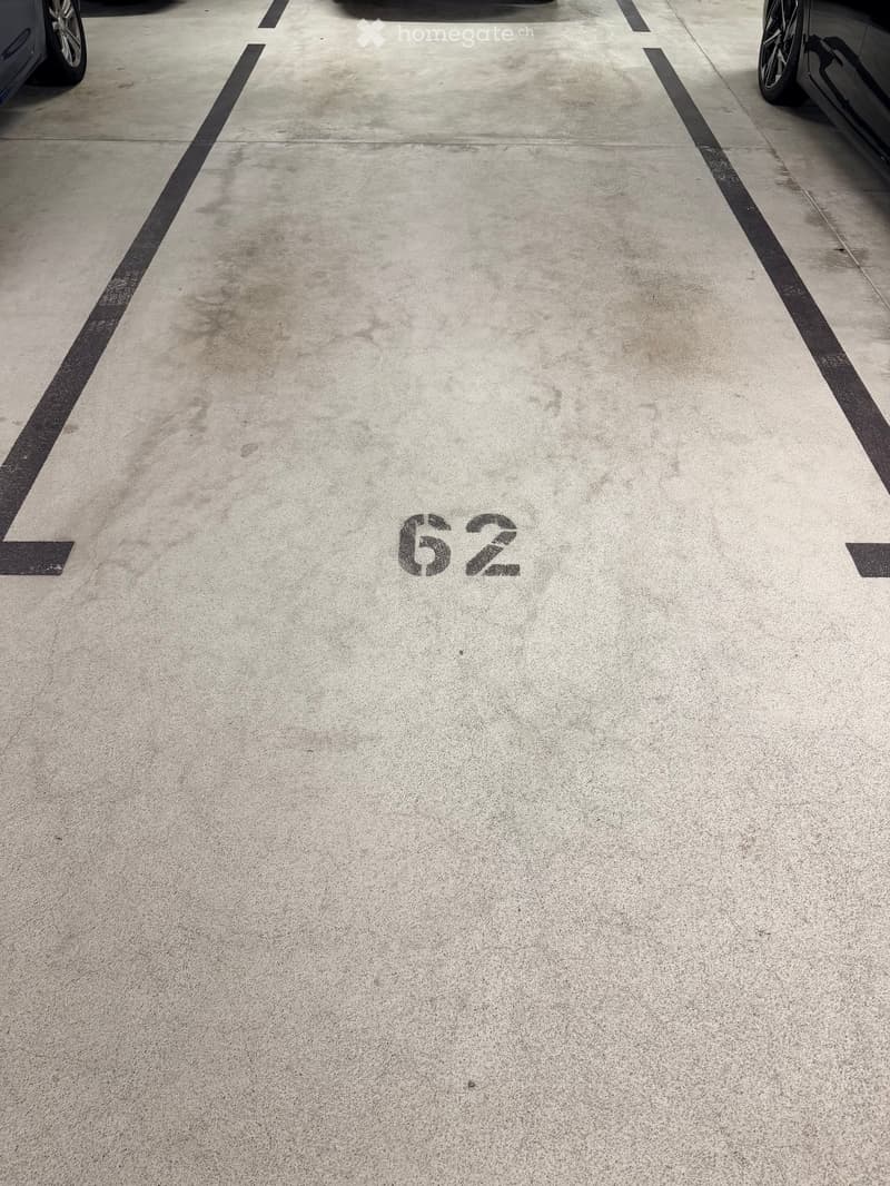 Parking space marked with number 62, concrete surface, partial view of cars at edges.