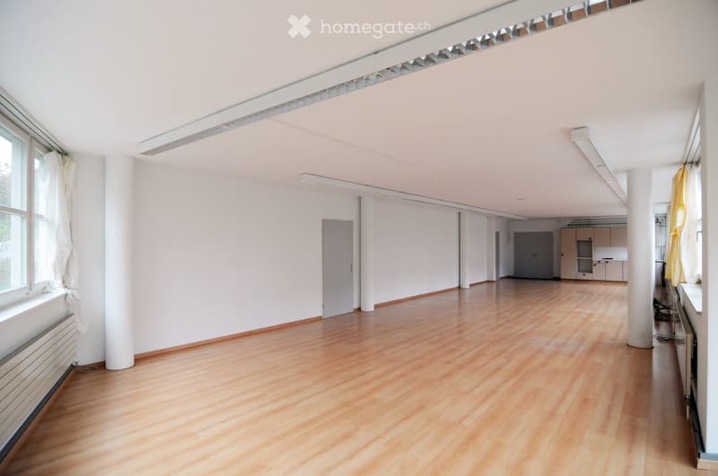 Empty room with wooden flooring, white walls, large windows, and a radiator. No furniture or equipment is present.