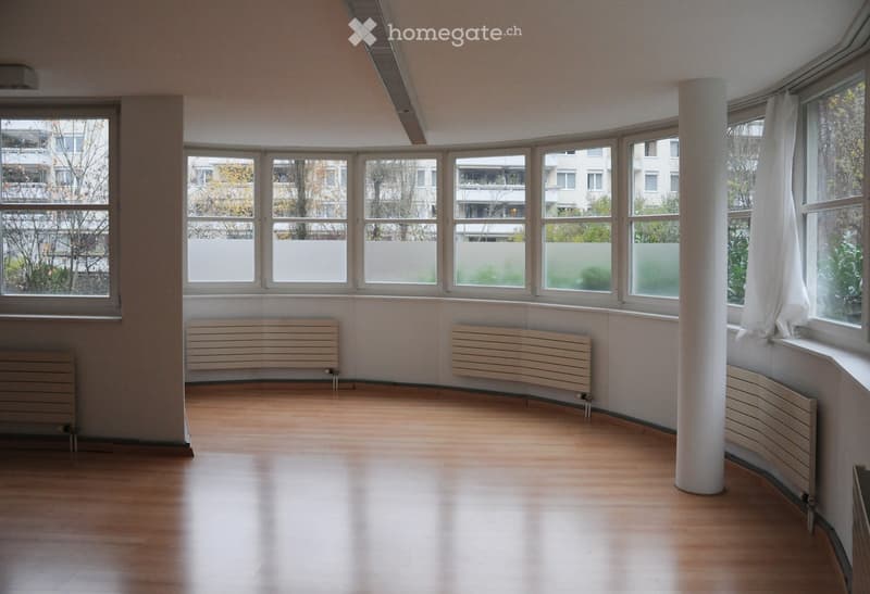 Empty room with wooden flooring, large windows, radiators, and a central white column.
