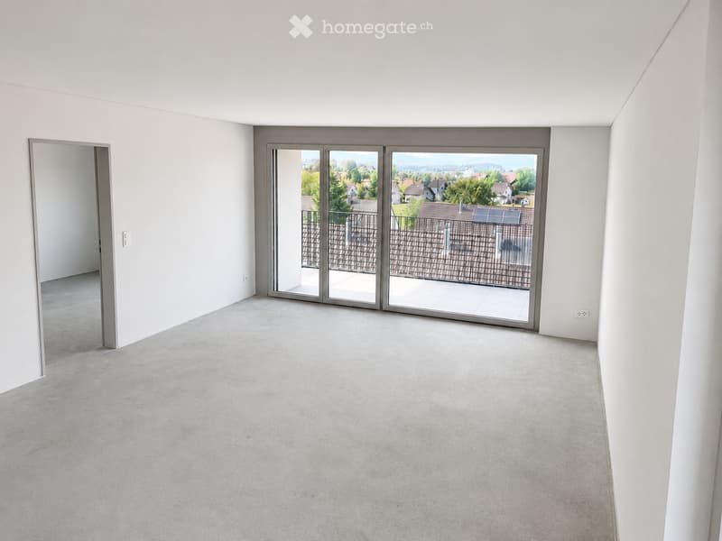 Empty room with white walls, concrete floor, large sliding glass doors leading to a balcony, and an open doorway to another space.