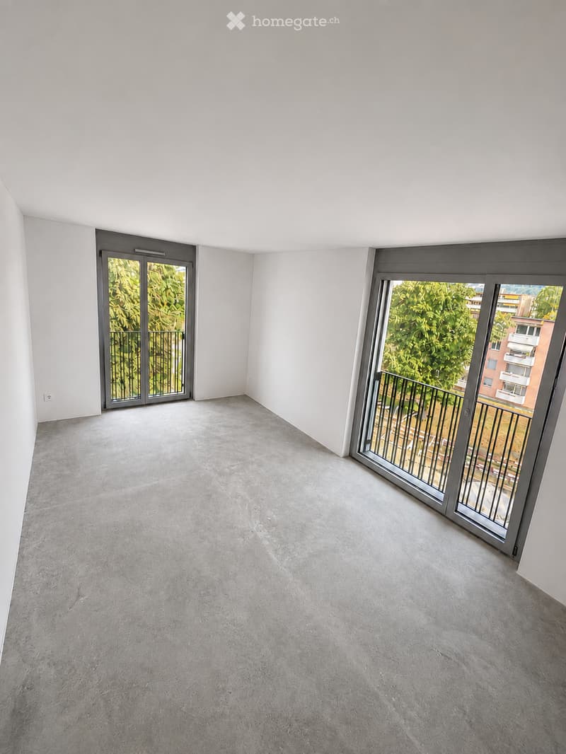 Empty room with grey concrete floor, white walls, and two large sliding glass doors leading to a balcony with metal railings.