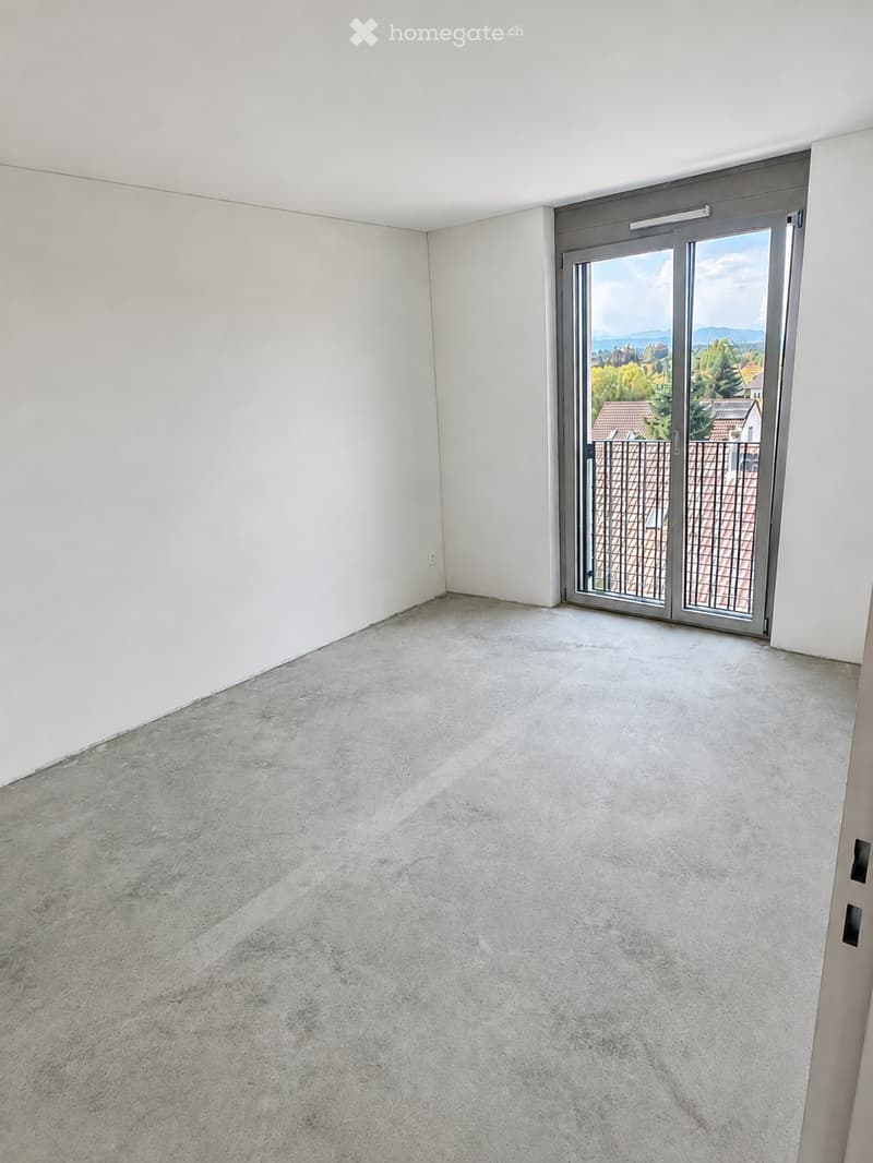 Empty room with white walls and a concrete floor, featuring a large sliding glass door leading to a balcony with a view of the landscape.