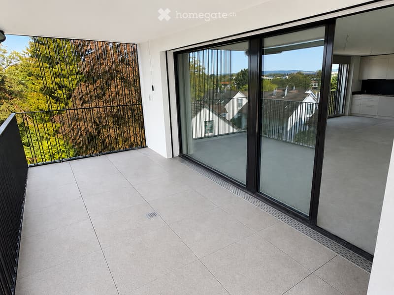 Modern balcony with large glass sliding doors, tiled floor, and metal railing offering a view of greenery and neighboring houses.