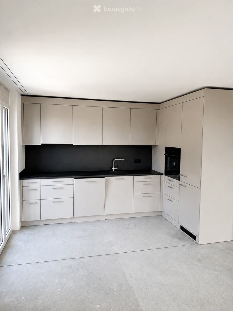 Modern kitchen with light-colored cabinets, white lower units, black countertop, and a single sink with a modern faucet.