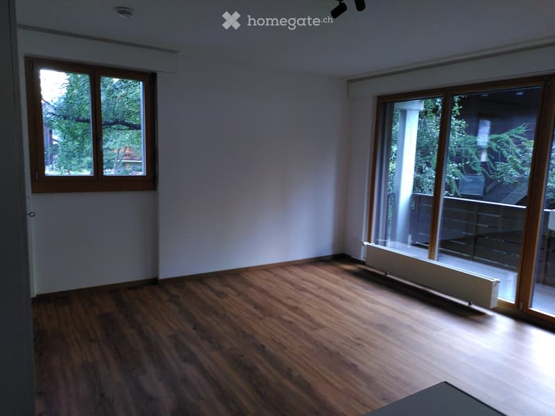 Empty room with wooden flooring, large windows, and sliding glass doors leading to a balcony or outdoor area.