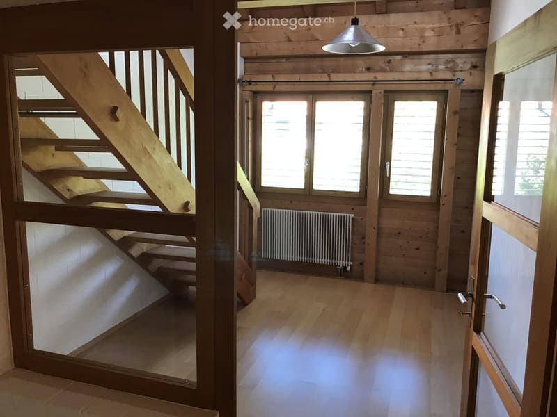 Bright, wooden-floored hallway with a staircase leading upwards, large windows, and a radiator visible in the background.
