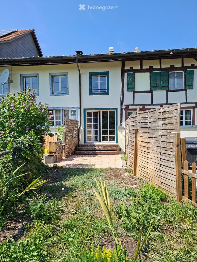 A garden area with a wooden fence, a small patio, and a house with multiple windows and shutters.