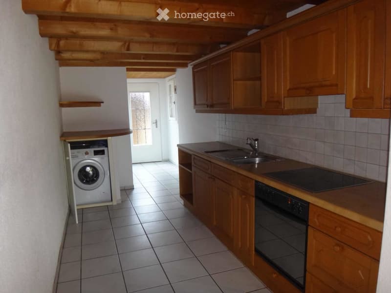 Bright kitchen with wooden cabinets, tiled floor, sink, oven, and washing machine tucked under the counter.