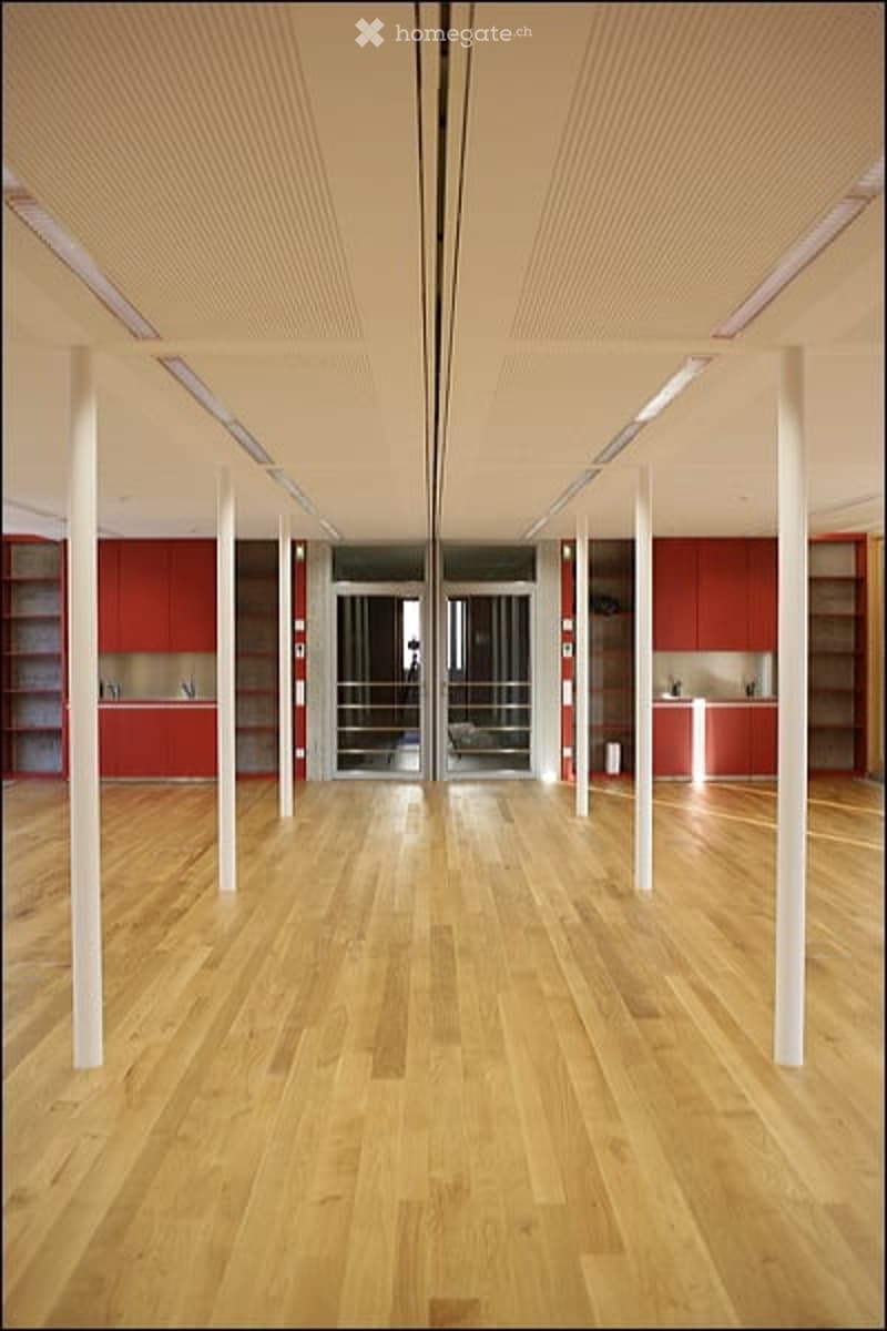 Open-plan space with wooden flooring, white columns, red cabinetry, and glass doors leading to another area.