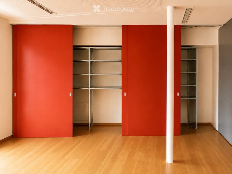 Empty room with wooden flooring, beige walls, and built-in storage units with red panel doors.