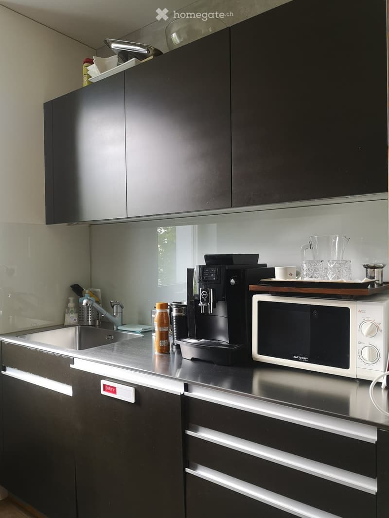 Modern kitchen with black cabinets, stainless steel sink, coffee machine, microwave, and various kitchen items on the counter.