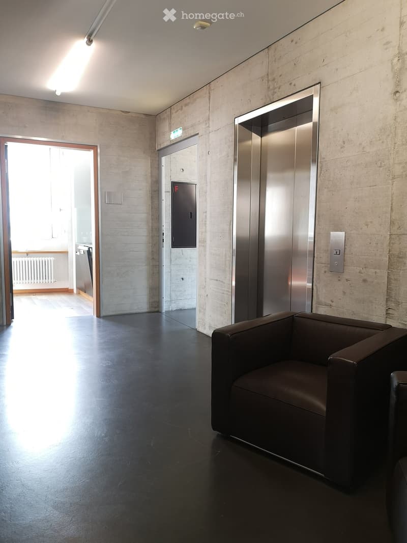 Modern, minimalist hallway with dark polished floor, leather sofa, elevator, and open doorway leading to another room.