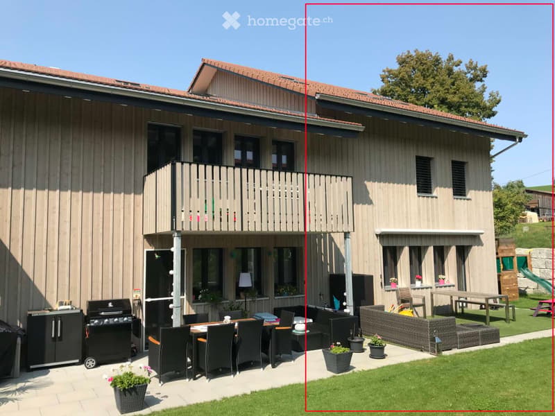 Modern two-story house with a balcony, patio seating area, and garden. Features include a dining set, outdoor furniture, and potted plants.