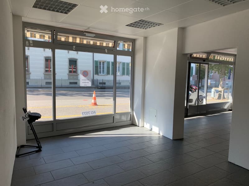 Empty room with tiled floor, large windows, and a small stand with a sign. No furniture or equipment present.