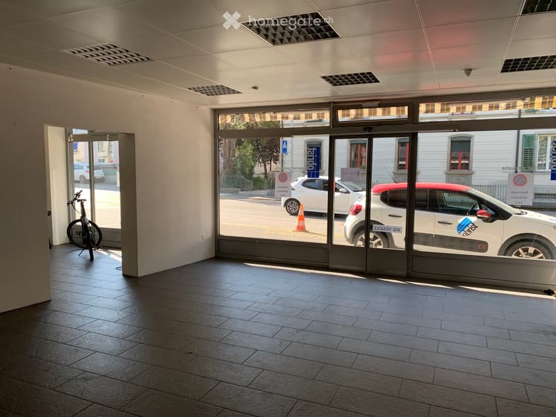Empty room with tiled floor, large glass doors leading to a street, and a bicycle leaning against a pillar.