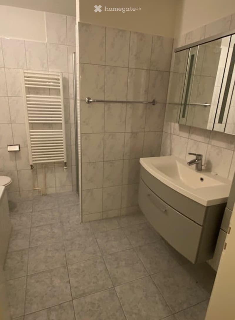 Modern bathroom with beige tiled walls and floor, white radiator, sink with mirror, and toilet.