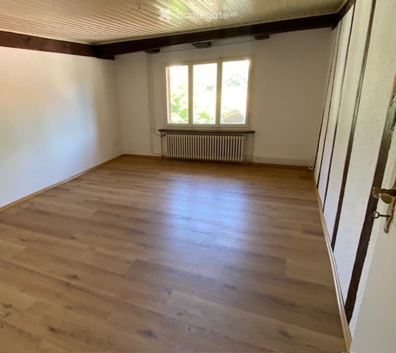 Empty room with wooden flooring, white walls, a single window, and a radiator below it. No furniture or equipment present.