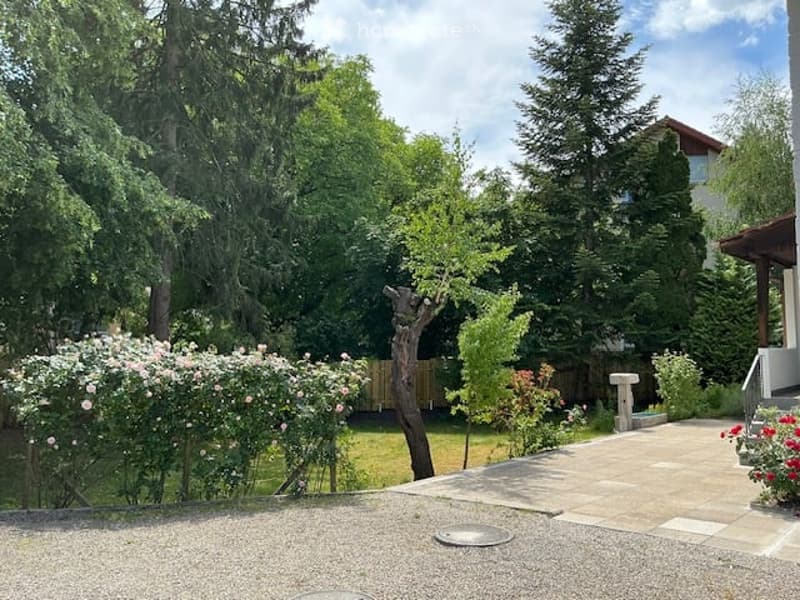 Well-maintained garden with a variety of trees, shrubs, and flowering plants, featuring a stone pathway and a small seating area.