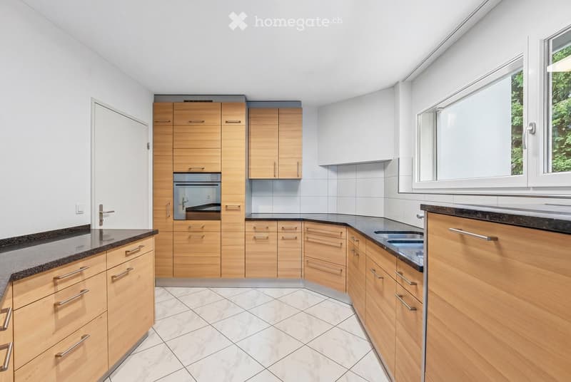 Modern kitchen with light wooden cabinets, granite countertops, and a built-in oven. The space features white tiled walls and a tiled floor.
