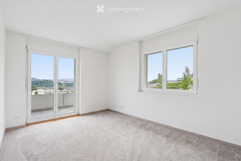Empty room with white walls, carpeted floor, large windows, and sliding glass doors leading to a balcony.