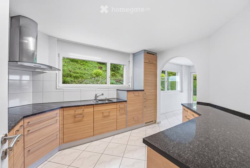 Modern kitchen with light wooden cabinets, stainless steel range hood, granite countertops, and a sink with a modern faucet.