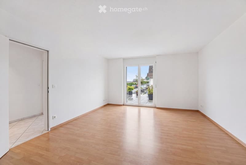 Empty room with light wooden flooring, white walls, and a large sliding glass door leading to an outdoor area.