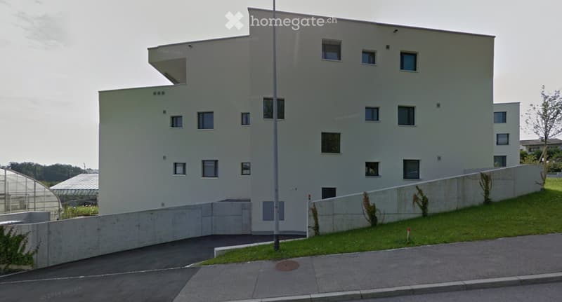 White modern building, 4 floors, raised ground floor, windows, concrete wall, grass