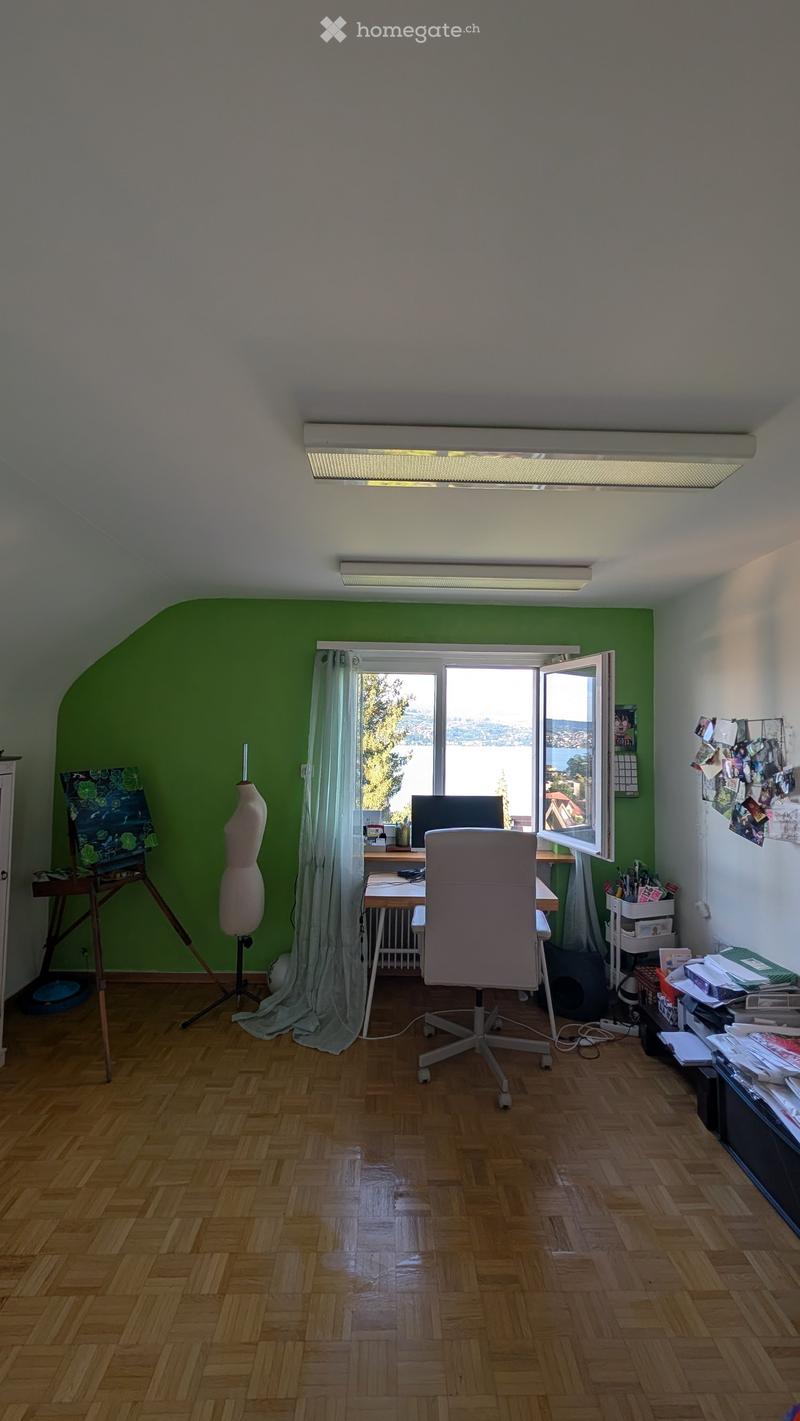 Bright room with wooden flooring, large window with view, desk with chair, computer, and various art supplies including an easel and mannequin.